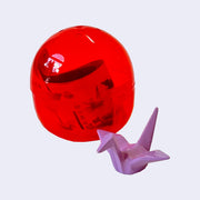 Bright red plastic capsule positioned behind a small figure modeled to look like a lilac purple origami crane.