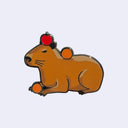 Enamel pin of a brown capybara, laying down with a red apple on its head and a tangerine on its back and between its paws.