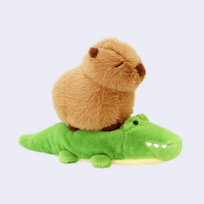 Fluffy stuffed animal of a capybara with closed eyes sitting atop of a cute smiling crocodile.