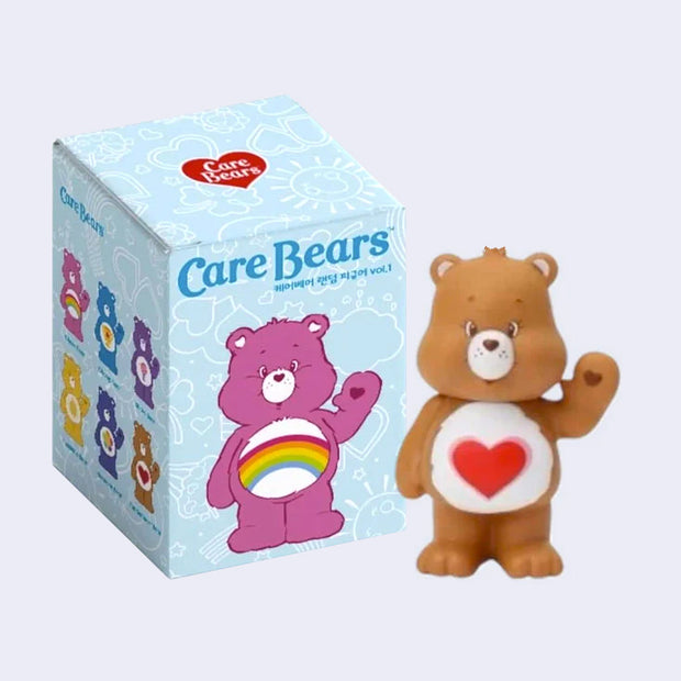 Brown vinyl figure of a Care Bears, standing with a heart on its stomach and waving. It stands next to its product packaging.
