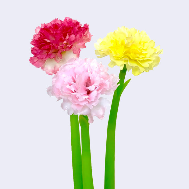 3 gel pens with a smooth green pen body and fluffy carnation flowers at the top, made out of some sort of fabric. Colors are red, pink or yellow.