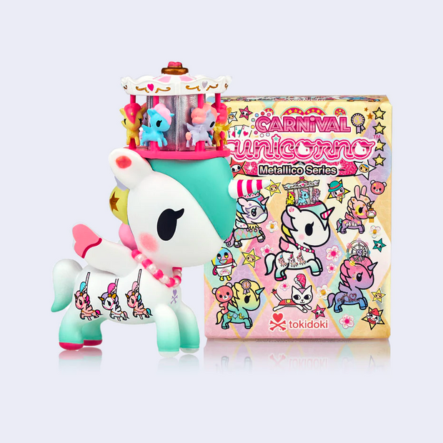 Plastic white unicorn with a small carousel atop of its head,  a striped horn and a pink necklace. It stands in front of its product packaging.