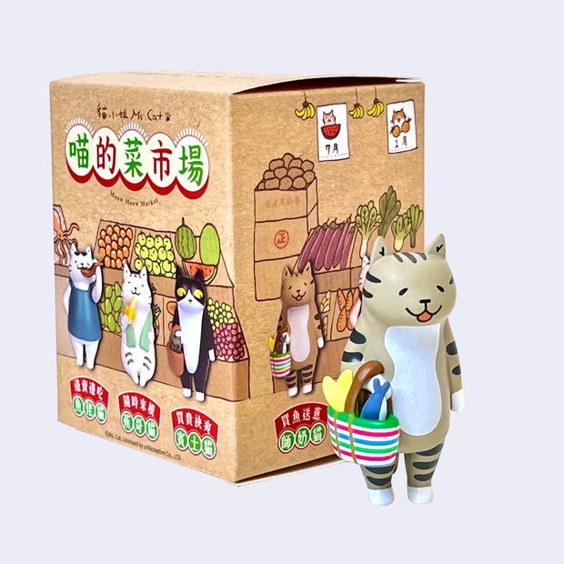 Vinyl figure of a striped cat with a cute, happy expression carrying a tote bag with groceries. It stands next to its product packaging with other shopping cats.