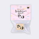 A packaged cat-themed rubber stamp set in a clear plastic bag with a pink backing card. The card has Japanese text and a black-and-white cat illustration, and the stamp itself shows a similar cat face design on a beige square block.