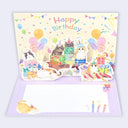 A 3D pop-up birthday greeting card featuring cute illustrated cats wearing party hats and gifts, with balloons, confetti, and the words 'Happy Birthday' on the back panel. The card is shown open against a light gray background.