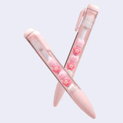 2 pink pens with clear bodies that show sakura flowers inside and small cat heads.