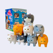 8 small plastic cats with flat backs and overall boxier bodies, standing atop of one another and assembling a pyramid like cheerleaders. They stand in front of their product box.
