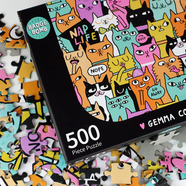 Jigsaw puzzle box with colorful cat illustrations and scattered pieces on a light background