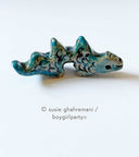 Ceramic sculpture of a dark green dragon with dips in its back for a place to put paintbrushes.