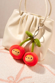 Plush cherry keychain with faces on a white bag