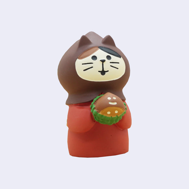 Sculpture of a small cat wearing a red kimono with a brown hood and holding a chestnut with a smiling face.