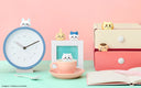 Cute room decor with a clock, desk, and various small items on a pink and green background.