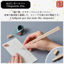 Chopsticks pen being used with a small container and paper on a gray background