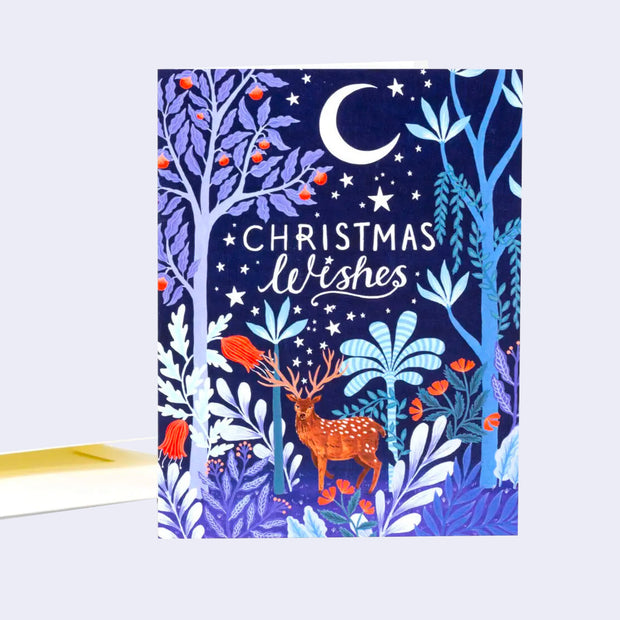 Greeting card, mostly dark blues and purples of an illustrated forest with a large buck in the center, under a crescent moon. Text reads "Christmas Wishes."