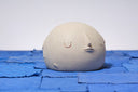 Carved wooden sculpture of a wide cream colored moon, with a flat bottom. It has several small craters and a closed eye, calm facial expression. 