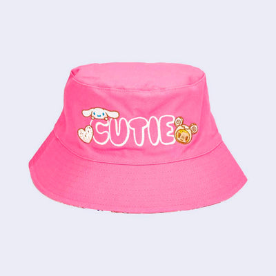 Hot pink bucket hat, featuring white bubble letters that read "CUTIE." Cinnamoroll is on one side and Donutella is on the other.