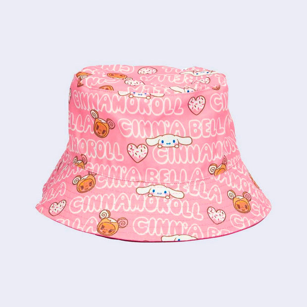 All over pattern on light pink bucket hat, with bubble letters spelling out "Cinnamoroll" and "Cinnabella." Small drawings of Donutella and Cinnamoroll are in between words.