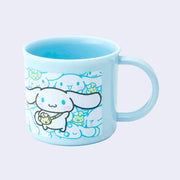 Small blue plastic cup with a mug handle featuring an illustration of Sanrio's Cinnamoroll, wearing a sling style bag shaped like a chick. Behind, is a patterned background of Cinnamoroll and a small yellow chick. 