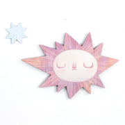 Sun-shaped wooden art piece with a face on a white background