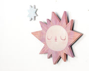 Sun-shaped wooden art piece with a face on a white background