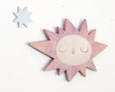 Sun-shaped wooden art piece with a face on a white background