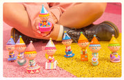 10 different designs and colorways of a vinyl figure featuring a boy sitting in or on some amusement park themed item. Items include: bumper car, stool, cannon, magician's hat, colorful stage, seal in a bowl, windup box, rocking chair or slide.
