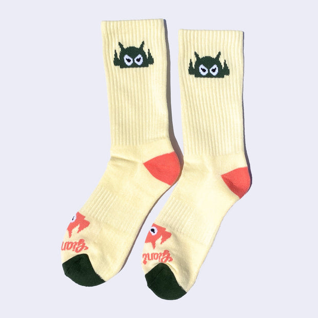 Cream color socks with a cartoon robot head on them and salmon pink colored heels and dark green toes. The robot head decorates the cuff end of each sock so that it peeks out when you wear sneakers.