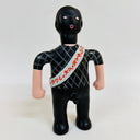 Toy figure with black hair, black and gray checkered shirt, and white sash with red text on a white background