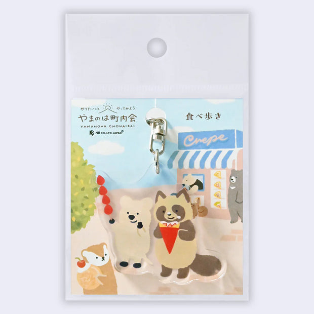 Keychain with cartoon raccoons on a scenic background, displayed on a white card.