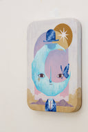 Painting of a suited person with a large crescent moon for a head, floating over its body. A bowler hat floats over the head and a butterfly rest on its face. Background is collage style of an archway sunset, mountains and a sun.