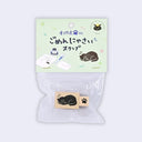 A packaged wooden stamp set with a light green header card and clear plastic bag. The stamp features a sleeping black cat illustration on a natural wood block, with the reverse side showing a black paw print.
