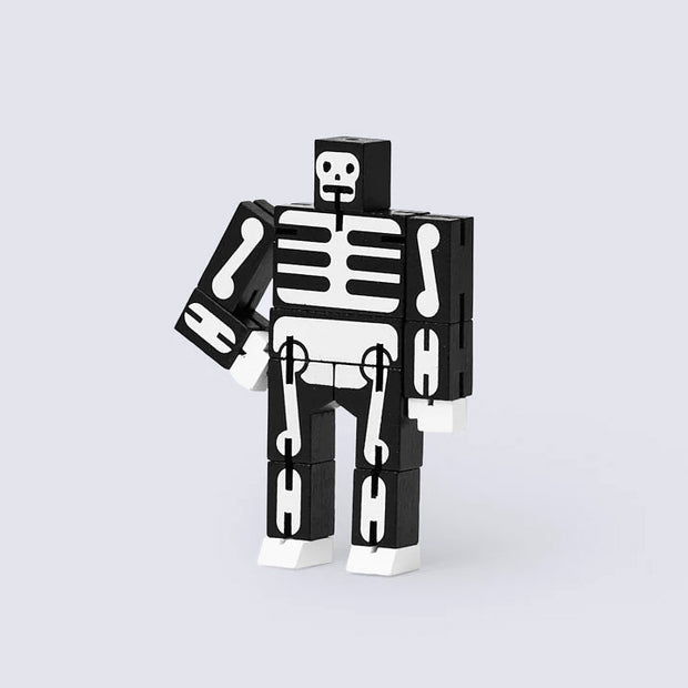 Wooden robot made out of many rectangular parts standing with its arms on its hips. Toy is painted black with white bone detailing.