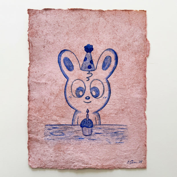 Blue colored pencil drawing of a cartoon bunny sitting in front of a cupcake.