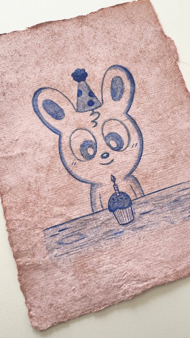 Blue colored pencil drawing of a cartoon bunny sitting in front of a cupcake.