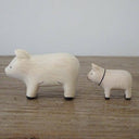 2 small white wooden figurines of pigs - one is larger than the other.