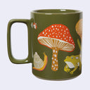 Olive green mug with illustrations of mushrooms, frogs and insects.