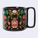 A glossy black ceramic mug featuring a vibrant, hand-painted style illustration of a ladybug surrounded by pink flowers and green leaves, set against a plain light gray background.