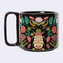 A glossy black ceramic mug featuring a vibrant, hand-painted botanical illustration of a beetle surrounded by pink flowers and green leaves, set against a plain light gray background.