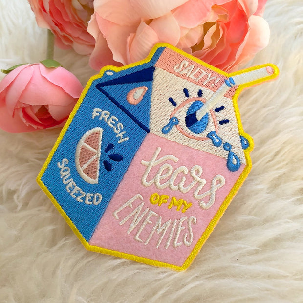 Die cut embroidered patch of a short carton of juice, with a white bendy straw poking out through an eye as the opening. Front reads "Tears of my enemies."