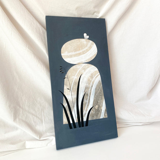 Collage style painting on solid dark gray background of a stack of 2 large rocks, with stark white and brown abstract marbling patterns. A white butterfly rests atop the top rock and a silhouette of tall grass is in front of the rock, bottom left. Displayed at an angle.