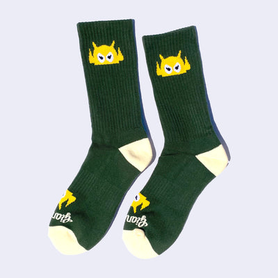 Dark green socks with a yellow cartoon robot head on them and cream colored heels and toes. The robot head decorates the cuff end of each sock so that it peeks out when you wear sneakers.