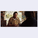 Two people in a room with vintage decor, one person facing the viewer and the other back turned.