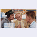 Three men in a room with cans of food, one of whom is wearing a police uniform.