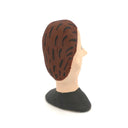 A hand-painted clay figurine of a man's head with brown hair, a beige face, black outlines, and a black shirt, shown against a plain white background.