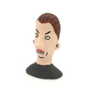 A hand-painted clay figurine of a man's head with brown hair, a beige face, black outlines, and a black shirt, shown against a plain white background.