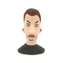 A hand-painted clay figurine of a man's head with brown hair, a beige face, black outlines, and a black shirt, shown against a plain white background.