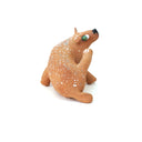 A small sculpted dog figurine in a warm tan-brown glaze with white speckles, a green eye, and a black nose, scratching behind its ear, photographed on a plain white background.