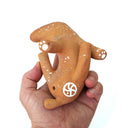 A hand holding a small brown ceramic animal figurine with white paw-print and circular cutout details, photographed against a plain white background.