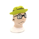 A handcrafted clay figurine of a man's head wearing a bright lime green hat and black-rimmed glasses with white circular lenses, set against a plain white background.
