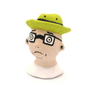 A handcrafted clay figurine of a man's head wearing a bright lime green hat and black-rimmed glasses with white circular lenses, set against a plain white background.